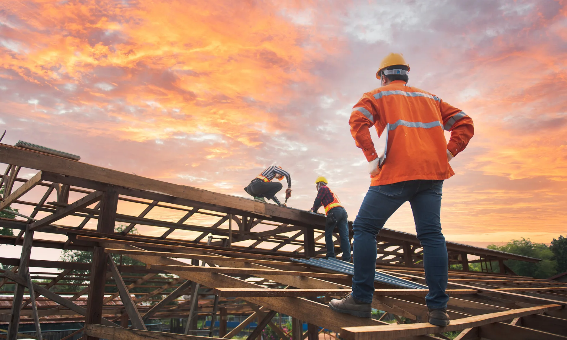 Worker wearing a hard hat and high-visibility vest on a construction site at sunset